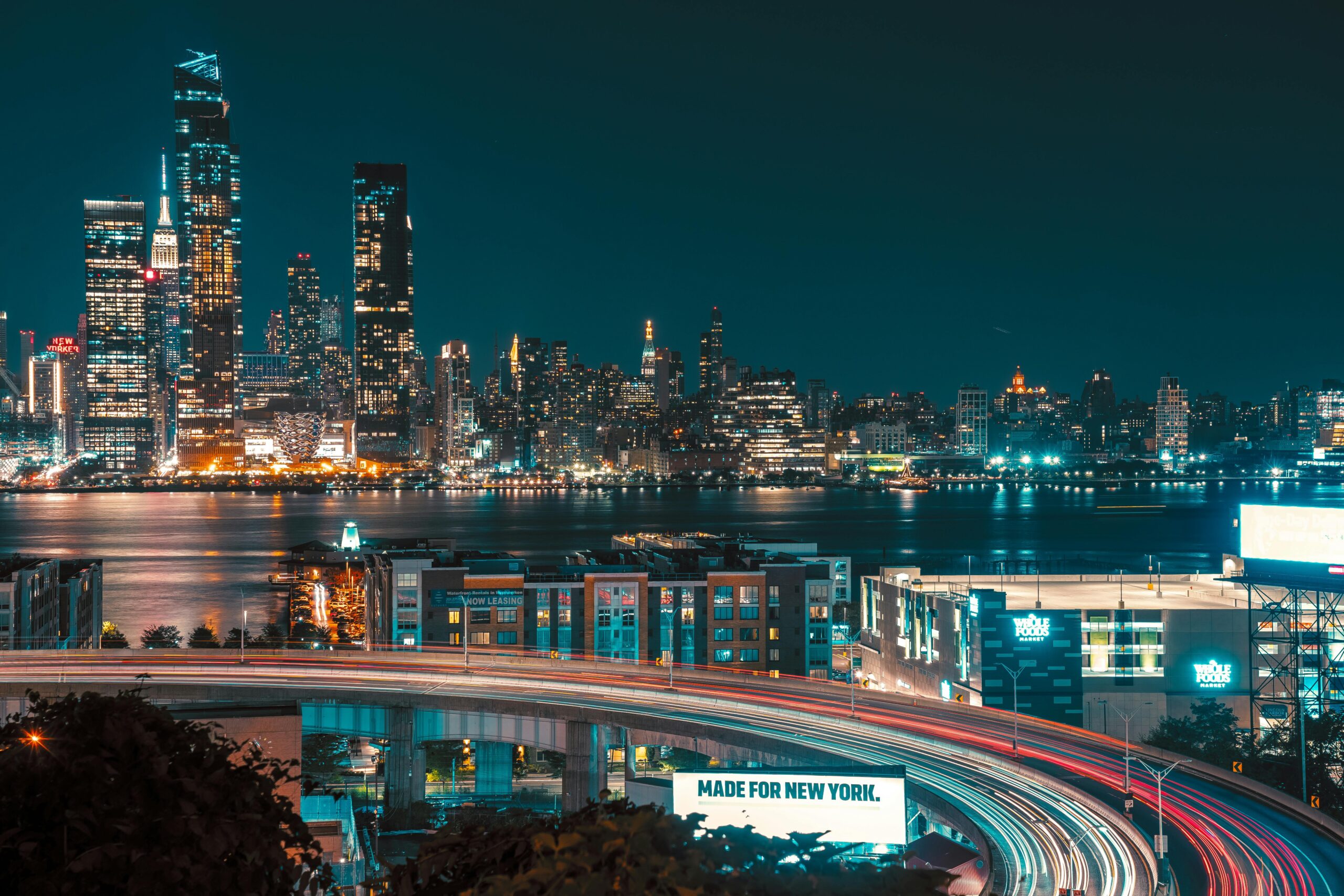A stunning night view of New York City's skyline with illuminated skyscrapers and a bustling highway.