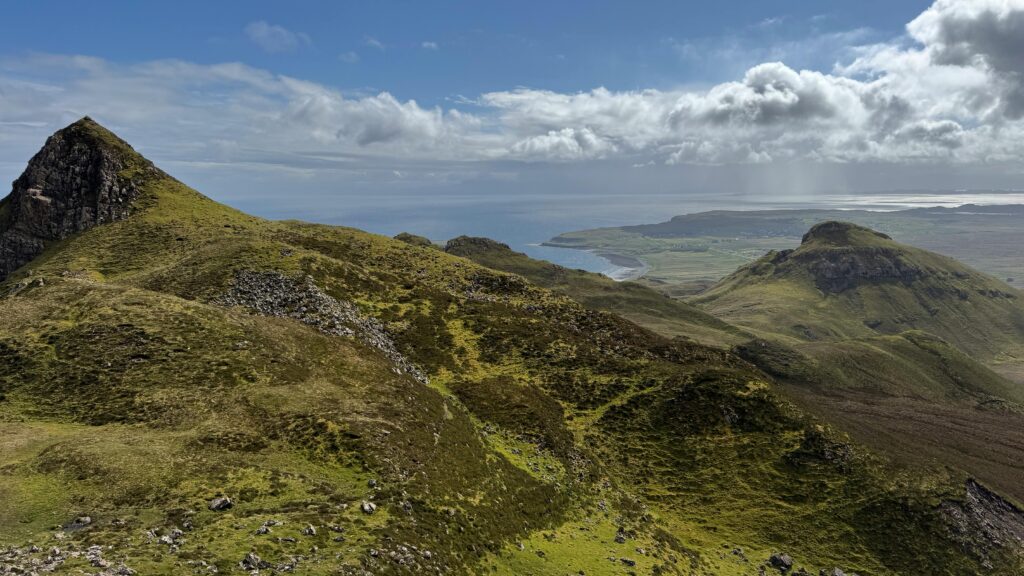 Breathtaking landscape of Quiraing on Isle of Skye, Scotland, featuring rolling hills and scenic ocean views under a partly cloudy sky.