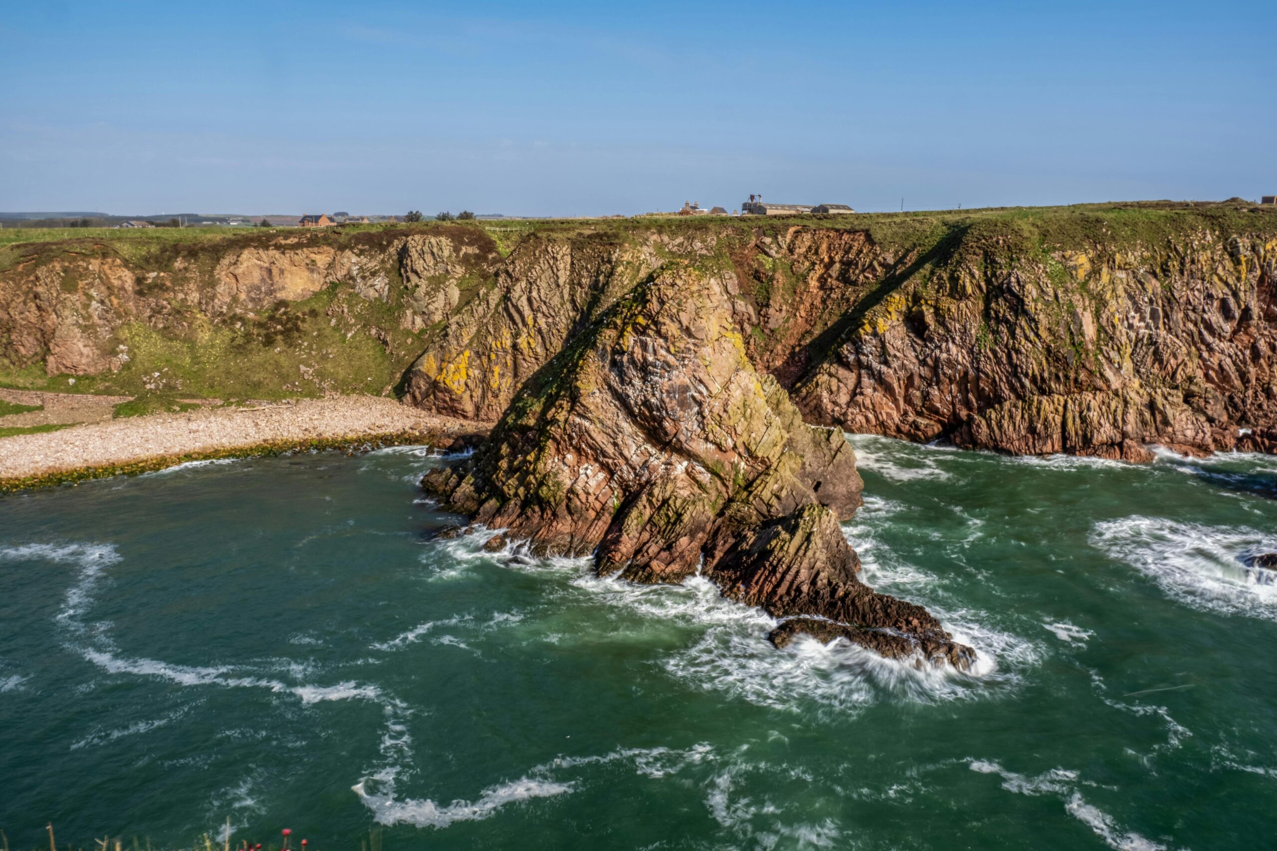 Stunning coastal cliffs with ocean waves crashing against the rocks under a clear blue sky.