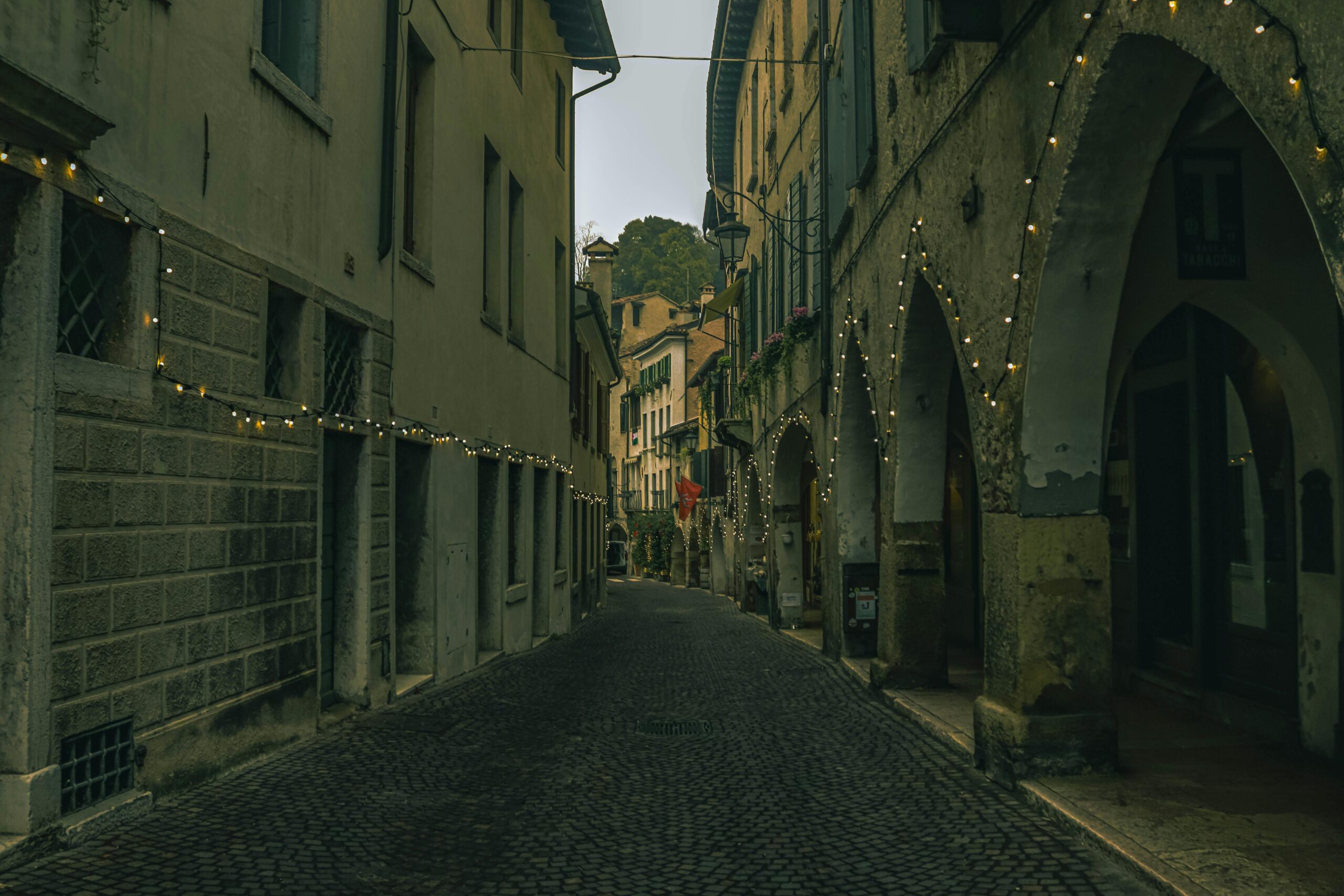 A picturesque narrow Italian street adorned with festive string lights, exuding historical charm.