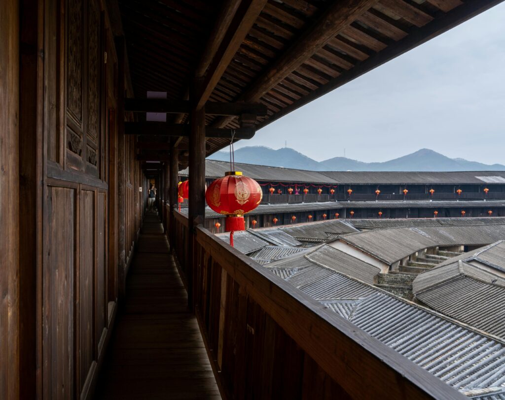Inside view of a traditional Chinese Tulou with red lanterns and mountainous background, showcasing cultural architecture.