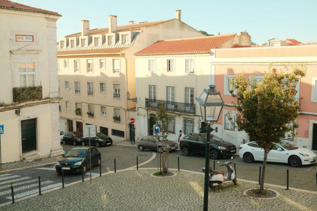 Warm sunny street scene in Lisbon's historic district, featuring classic architecture and parked cars.
