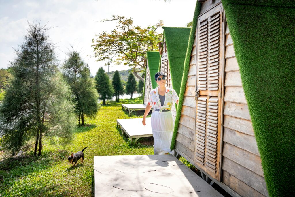 Woman with dog walking by unique countryside cabins in sunny outdoor setting.