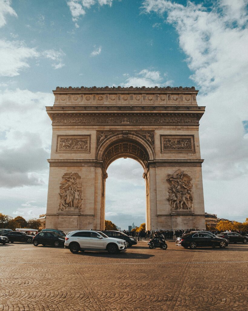 Beautiful view of the Arc de Triomphe surrounded by vehicles under a blue sky in Paris.