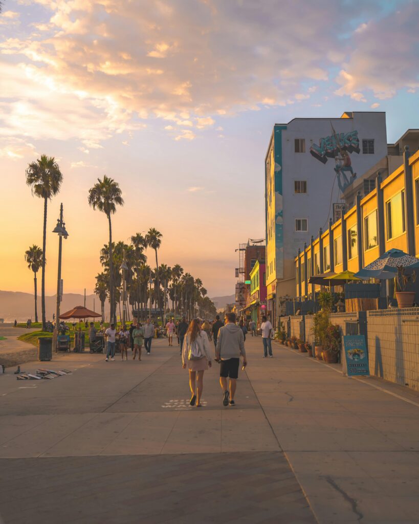 Tourists enjoying a calm evening stroll on the picturesque Venice Beach boardwalk at sunset.