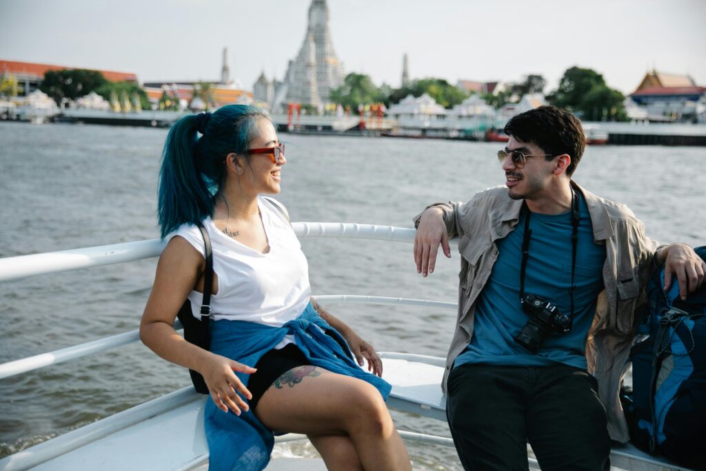 Tourists smiling and chatting on a ferry in Bangkok with a temple view.