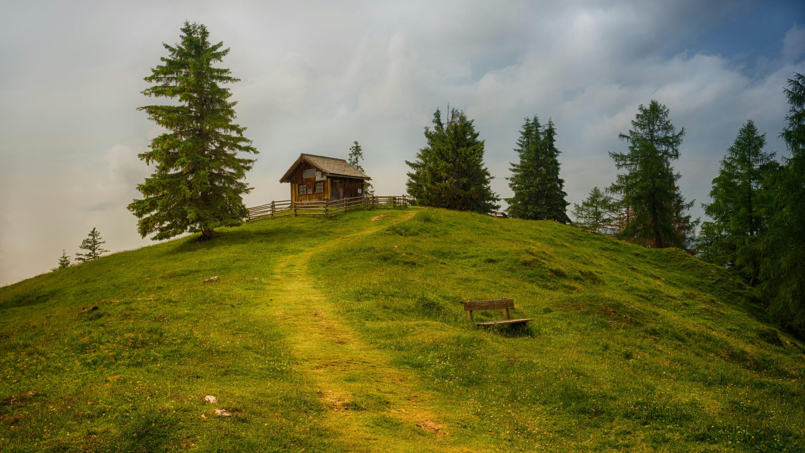 A picturesque cabin on a grassy hill surrounded by trees under a cloudy sky