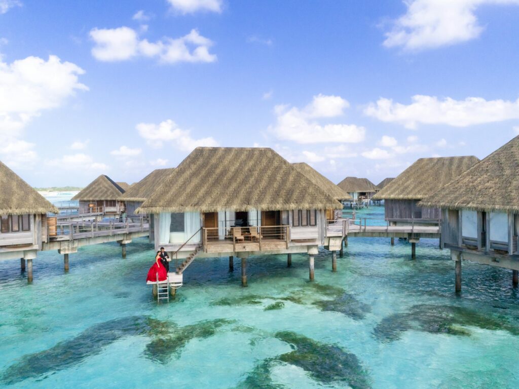 Overwater villa with couple in red dress in a tropical paradise setting.