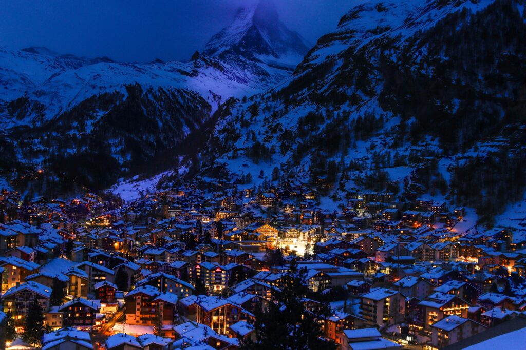 A captivating nighttime view of Zermatt, Switzerland, with illuminated houses and snow-covered mountains.