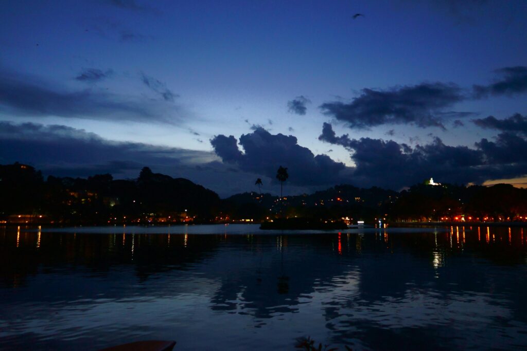 A serene dusk scene over Kandy Lake with vibrant reflections and silhouettes.