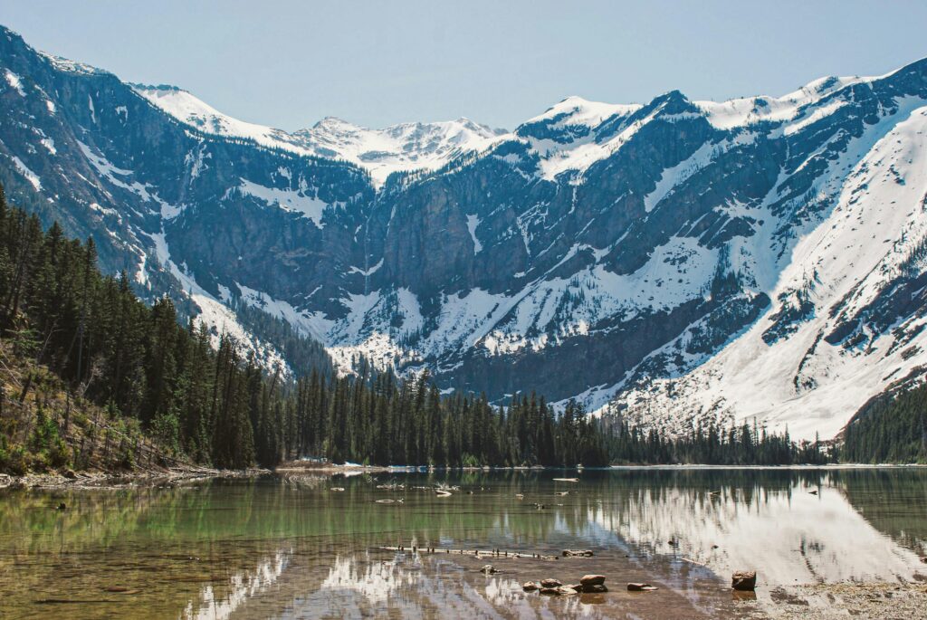 Breathtaking view of a tranquil lake with snowy mountains and coniferous forest in the background.