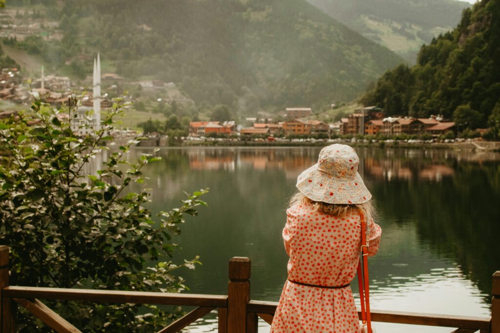 A woman in a sundress and hat stands by a lake, enjoying the scenic mountain town view.