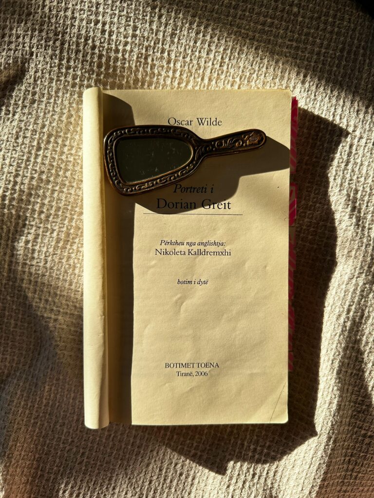 An open book with a vintage hand mirror on a burlap surface in sunlight.