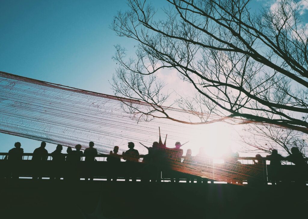 People silhouetted on a bridge in Tokyo against a bright sunrise, with tree branches framing the scene.