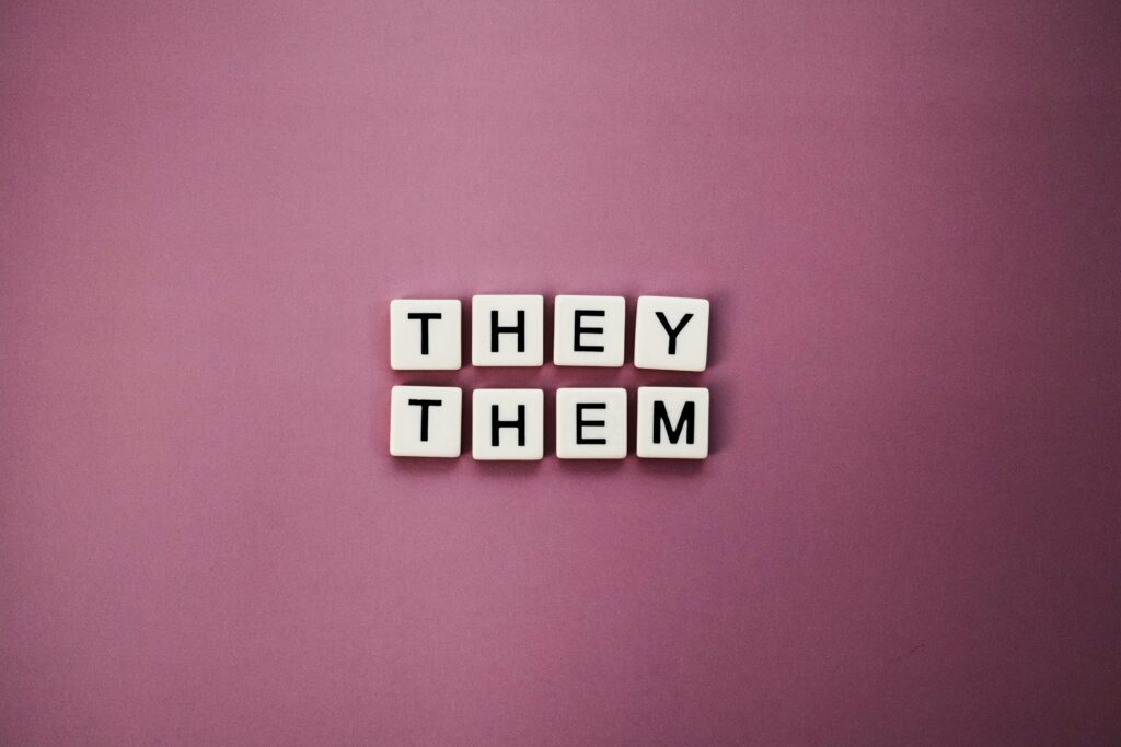 Non-binary pronouns 'they them' displayed with letter tiles on a pink backdrop.