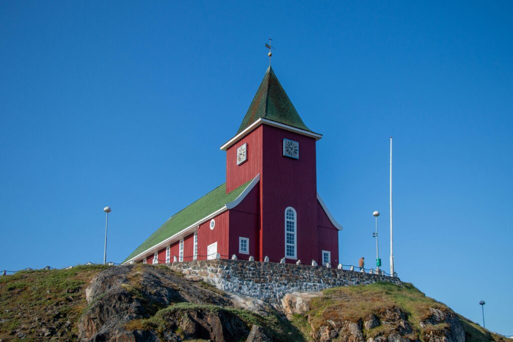 A stunning view of a historic red church in Sisimiut, Greenland against a clear blue sky.