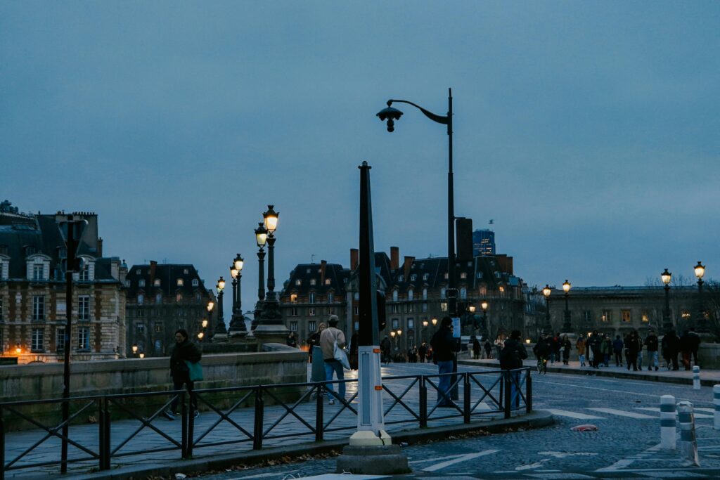 People walking on a Paris street in the evening under street lights.