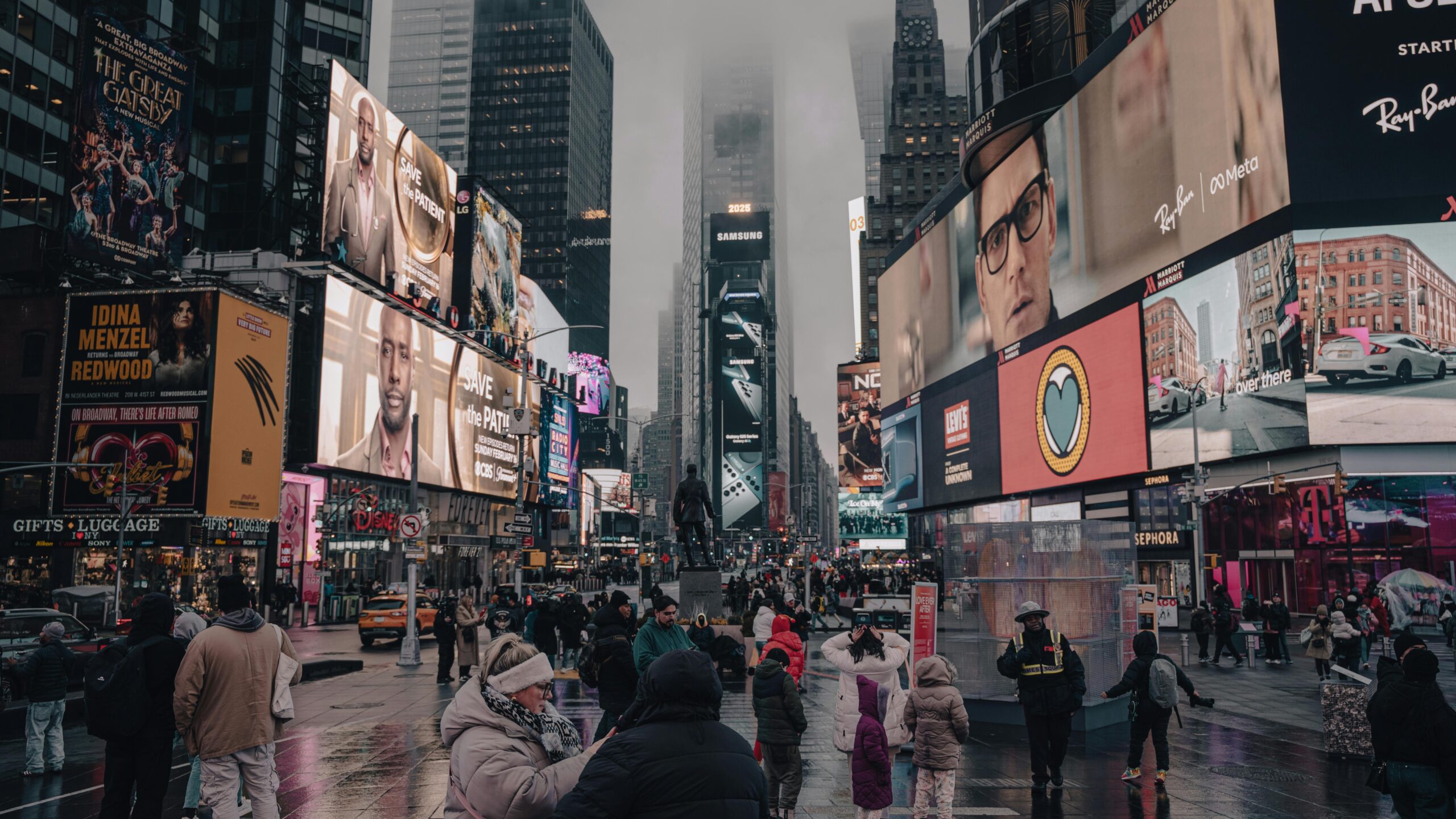 Crowds at Times Square surrounded by towering billboards and skyscrapers on a cloudy day.