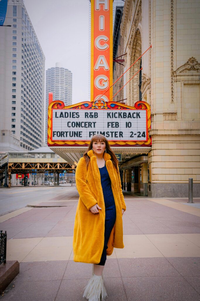Fashionable woman in yellow coat at Chicago Theater, winter scene.