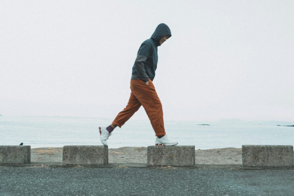 A person walks along the seaside in Chiba, Japan, wearing a hoodie and orange pants.