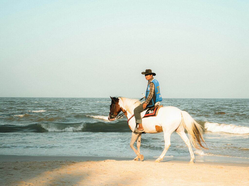 A man rides a horse along the beach in Thailand at sunrise, showcasing serene ocean views.