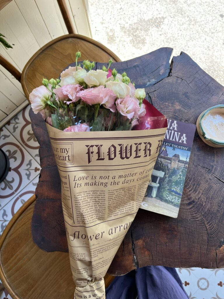 Delicate bouquet of flowers wrapped in vintage paper on a rustic table with book.