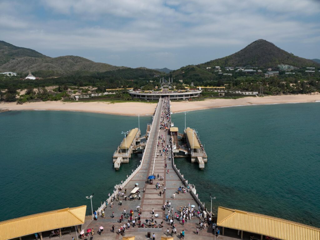 Explore Sanya's picturesque pier stretching into the ocean against lush mountains, perfect for travel enthusiasts.