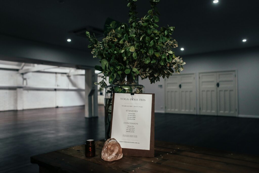 A tranquil yoga studio interior featuring a fee chart, decorative plant, and soft lighting.