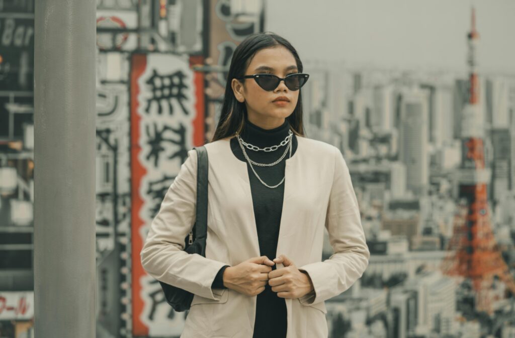 Fashionable woman in sunglasses posing in city with iconic tower backdrop.