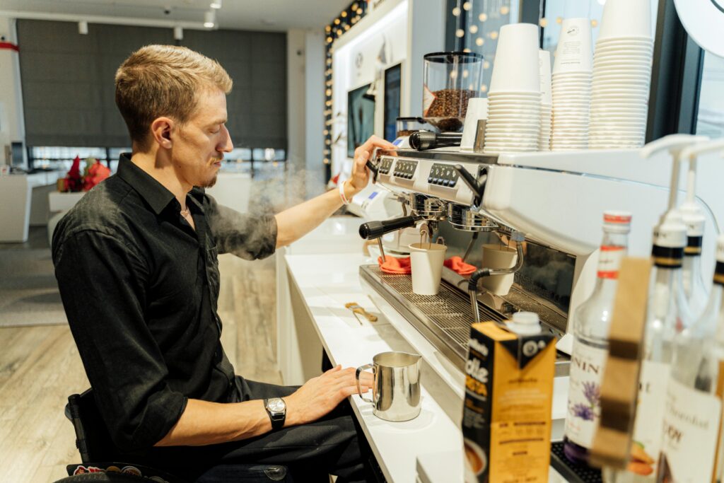 Barista in wheelchair using espresso machine to make coffee in a modern cafe setting.
