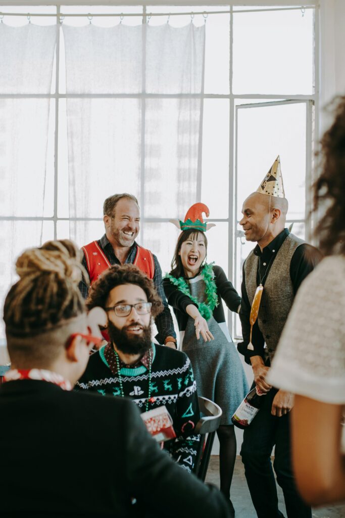 Group of coworkers celebrating holiday season in office with festive outfits and hats.