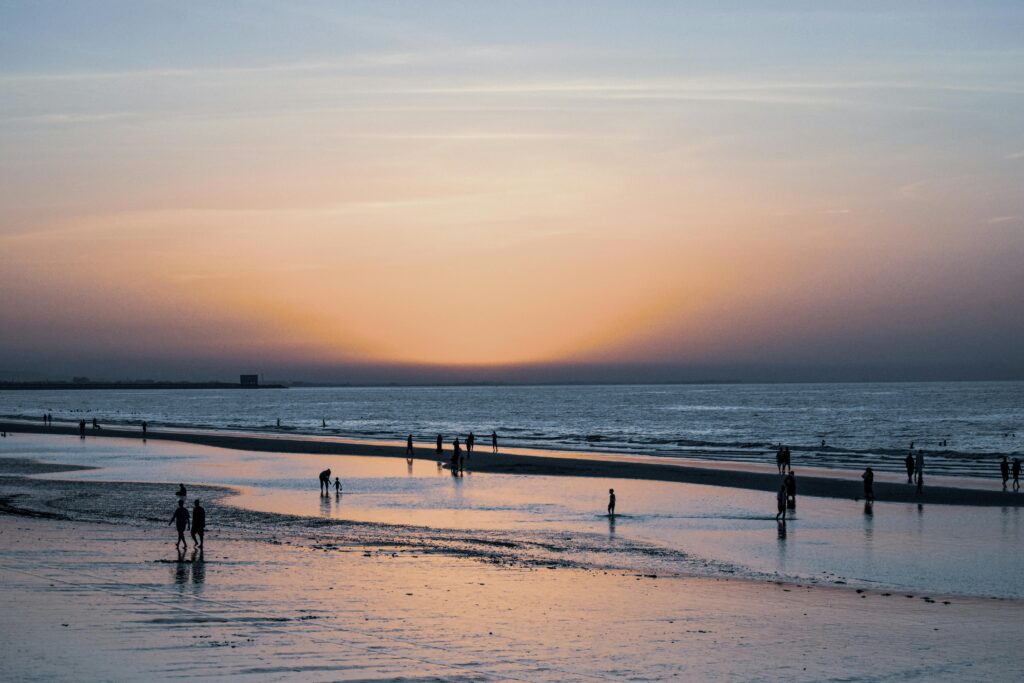 Silhouettes of people walking along a serene beach in Muscat during a vibrant sunset.