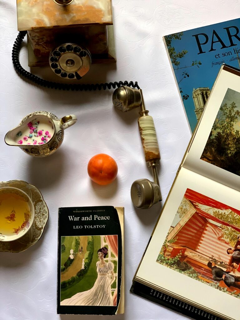 Elegant overhead shot of a vintage tea set with classic literature and assorted items on a white background.
