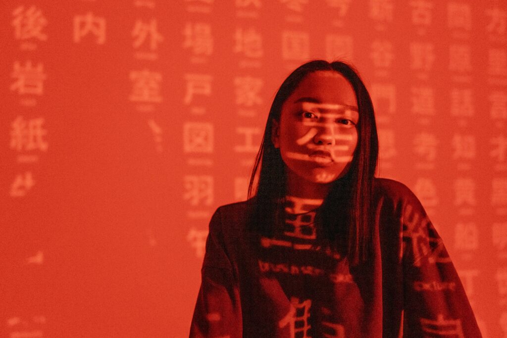 A woman with an expressionless face with Chinese calligraphy projected on a red background.