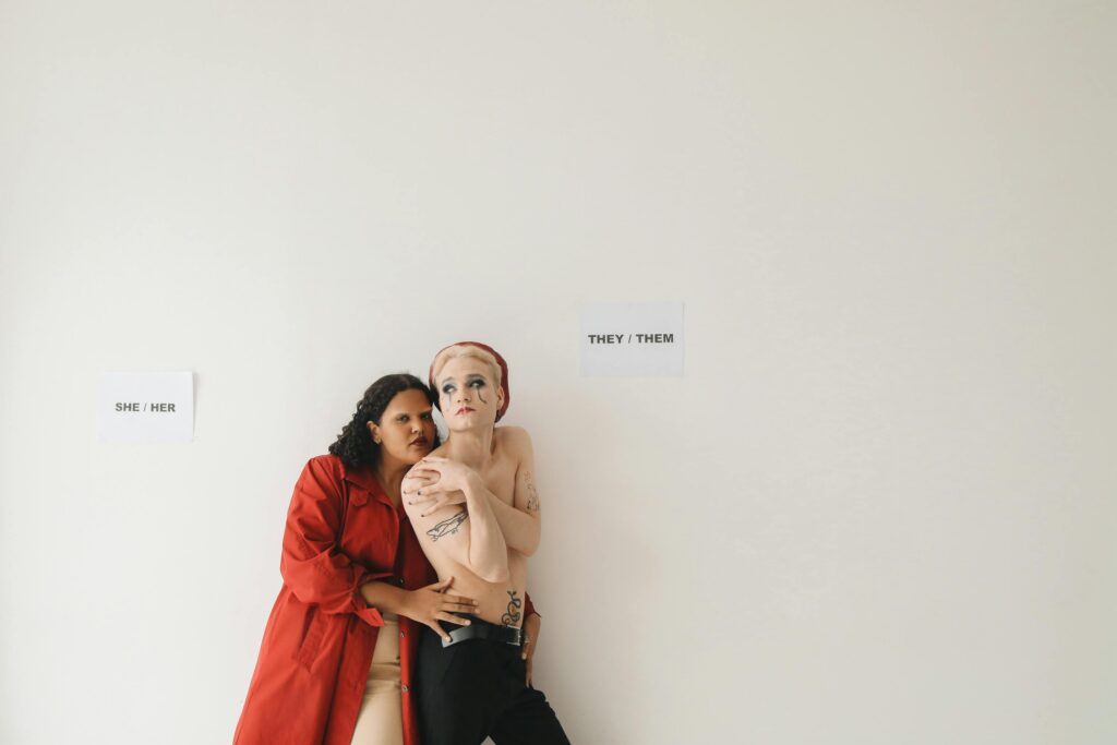 A studio portrait showcasing diverse fashion with two individuals expressing identity through pronouns.
