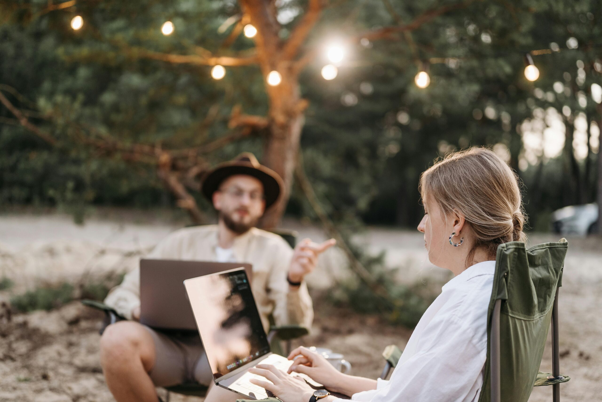 Two adults working on laptops in a rustic outdoor setting with ambient lighting.