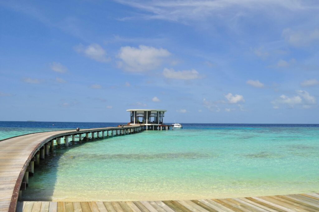 Beautiful tropical beach with a long wooden jetty stretching into the turquoise ocean in the Maldives.