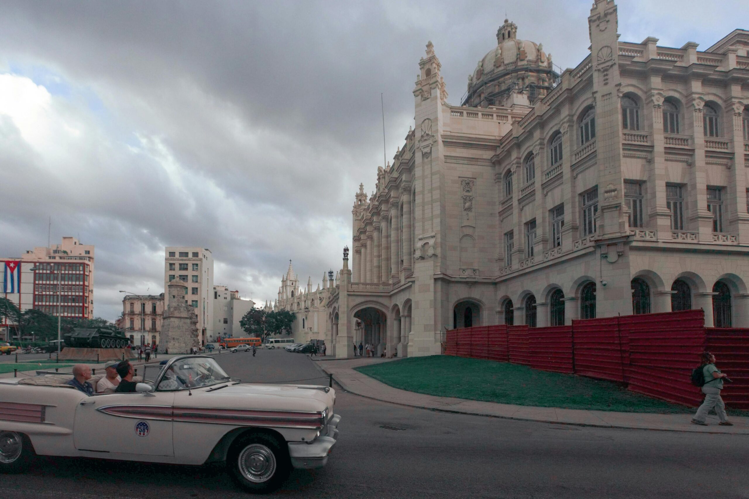 Vintage car driving past a historic building under cloudy skies in Havana, Cuba.