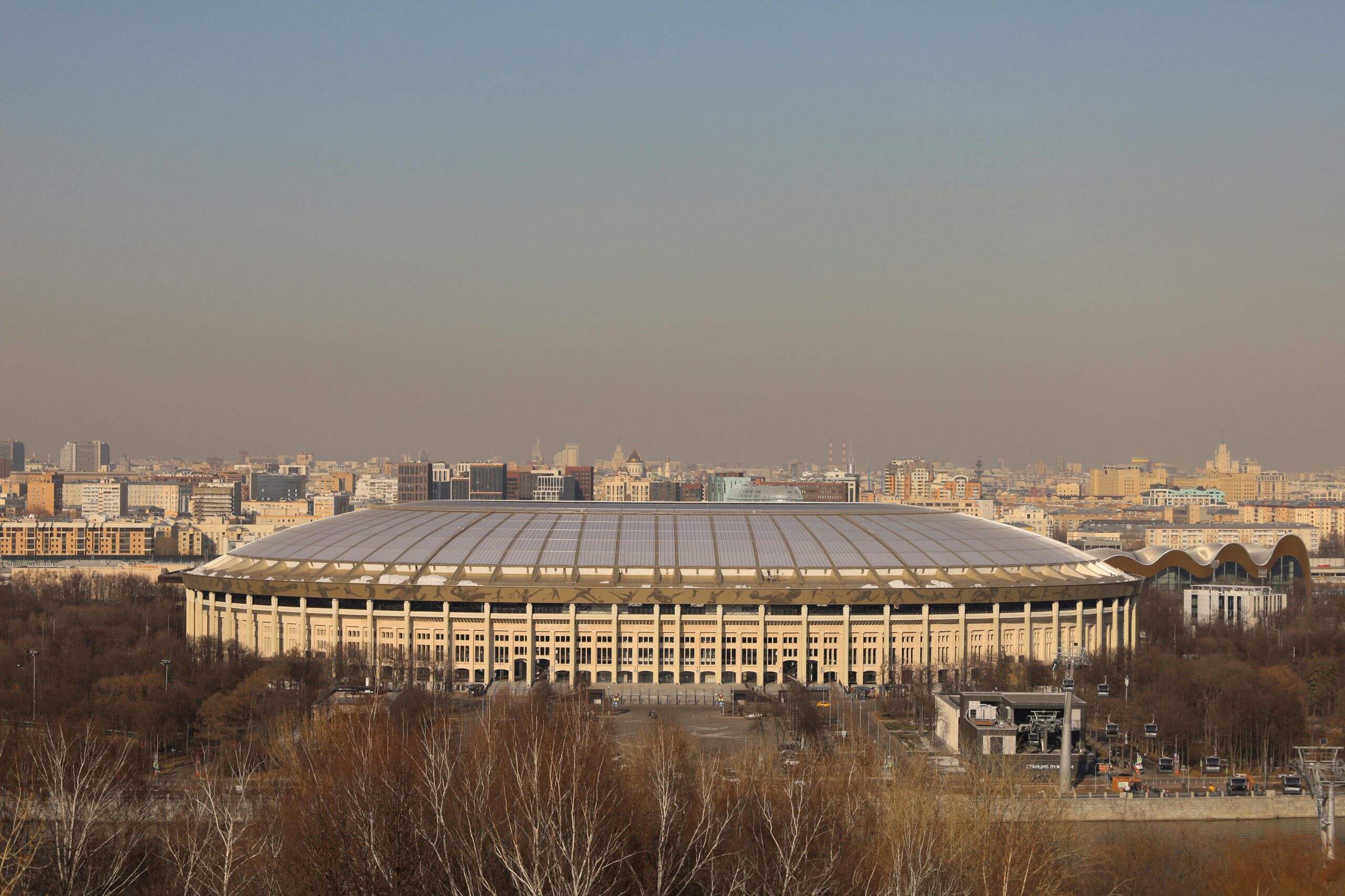 Aerial view of Luzhniki Stadium in Moscow with the city's skyline at sunset, showcasing urban architecture.