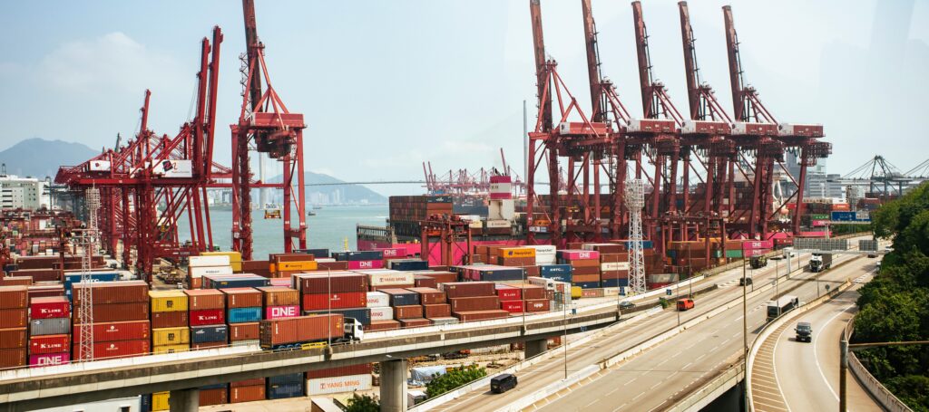 A vibrant view of Hong Kong's bustling shipping port with red cranes and stacked containers.