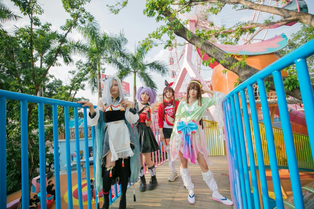 A group of cosplayers in vibrant costumes posing outdoors on a colorful footbridge in an urban park.