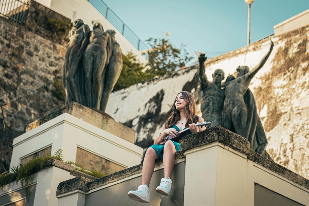 A young woman in a sundress plays the ukulele near statues in San Juan, Puerto Rico.