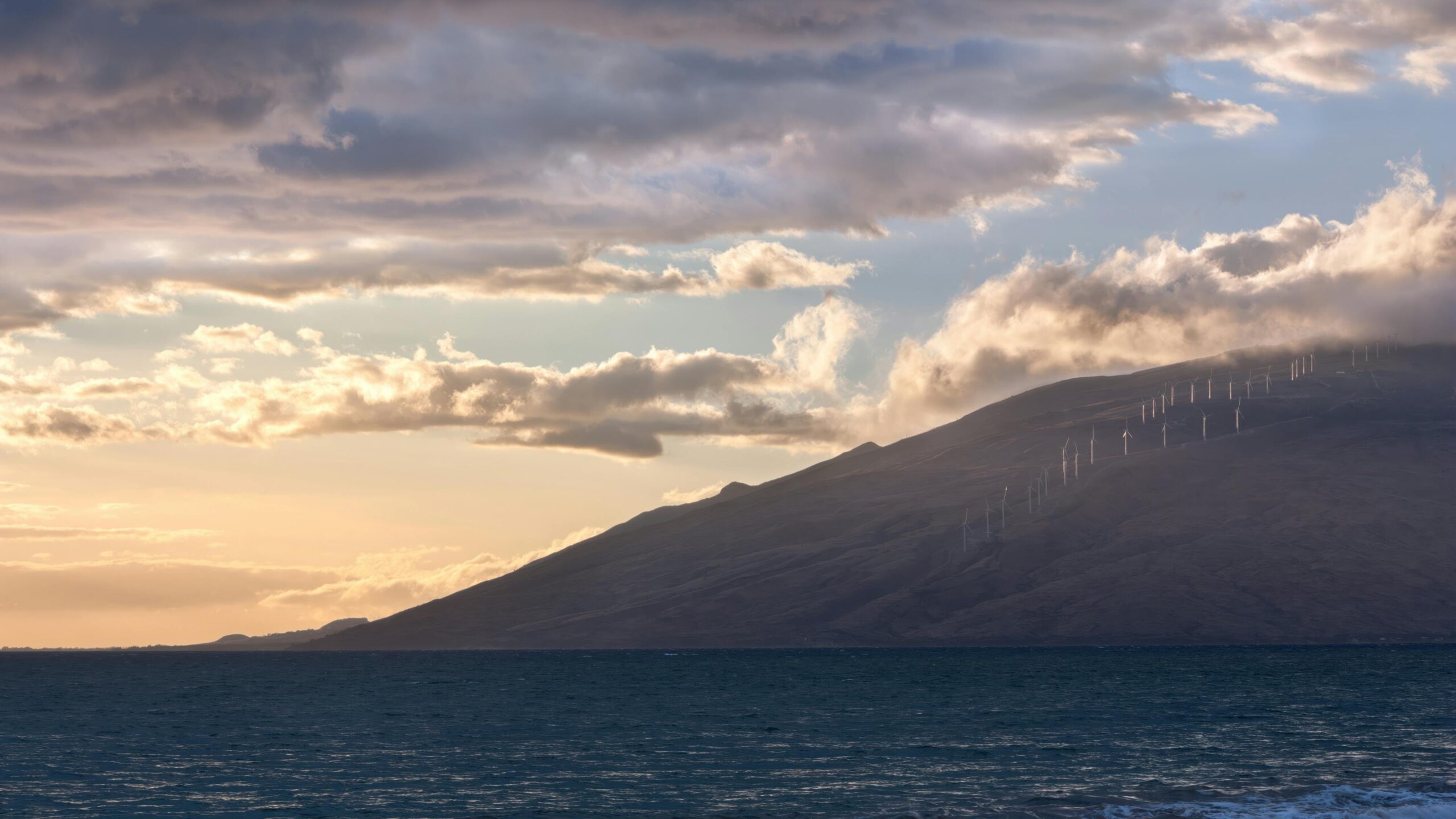 Serene sunset view over Kihei, Hawaii with wind turbines along the coast, capturing nature and renewable energy.