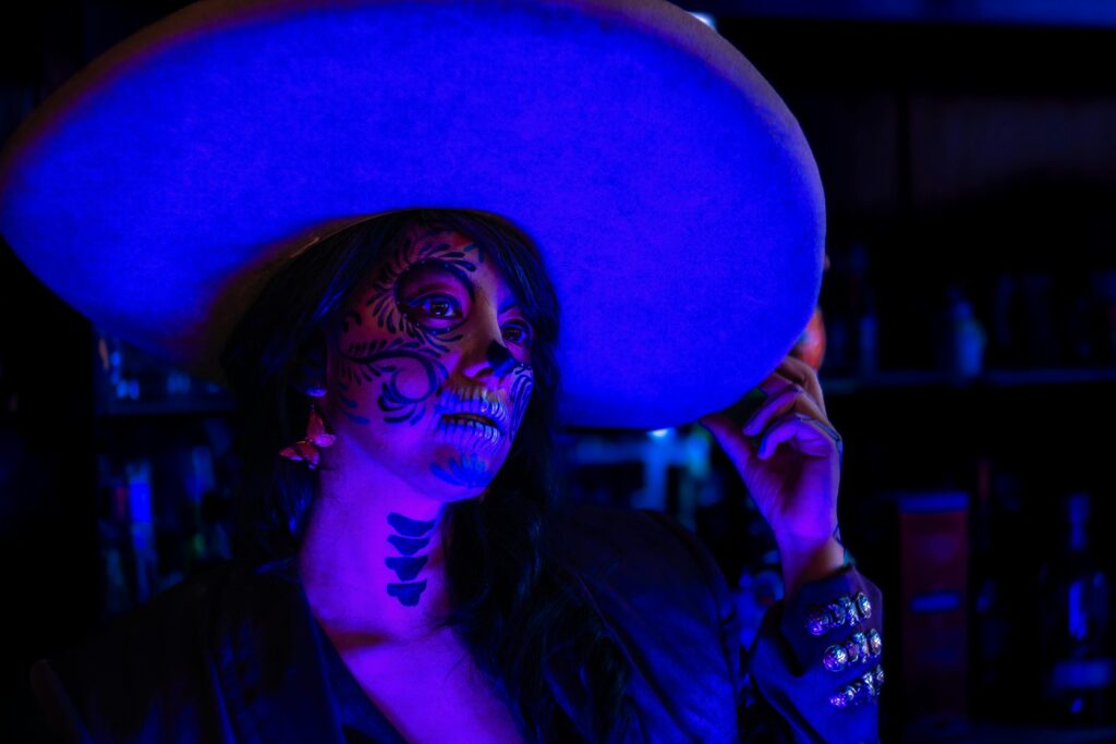 Vibrant Day of the Dead themed portrait with colorful makeup and traditional hat in a nightclub setting.