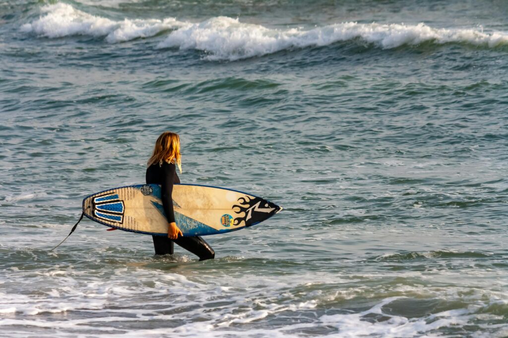 A woman carrying her surfboard enters the ocean waves in Lima, Peru, ready for a surfing adventure.