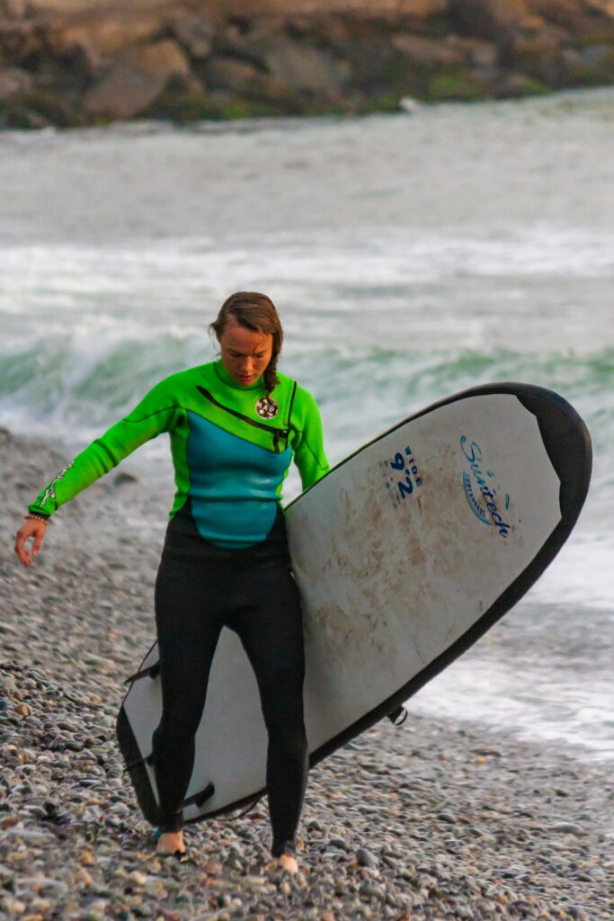 Woman in wetsuit carrying surfboard along a rocky beach in Lima, Peru.
