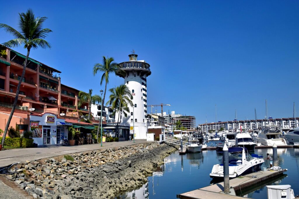 Scenic view of Marina Vallarta lighthouse and waterfront boats under a clear blue sky.