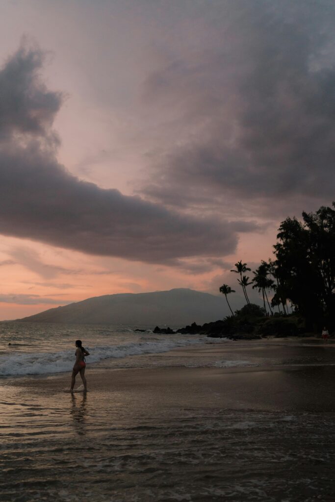 A tranquil beach scene at sunset in Kihei, Hawaii, with palm trees and ocean waves.