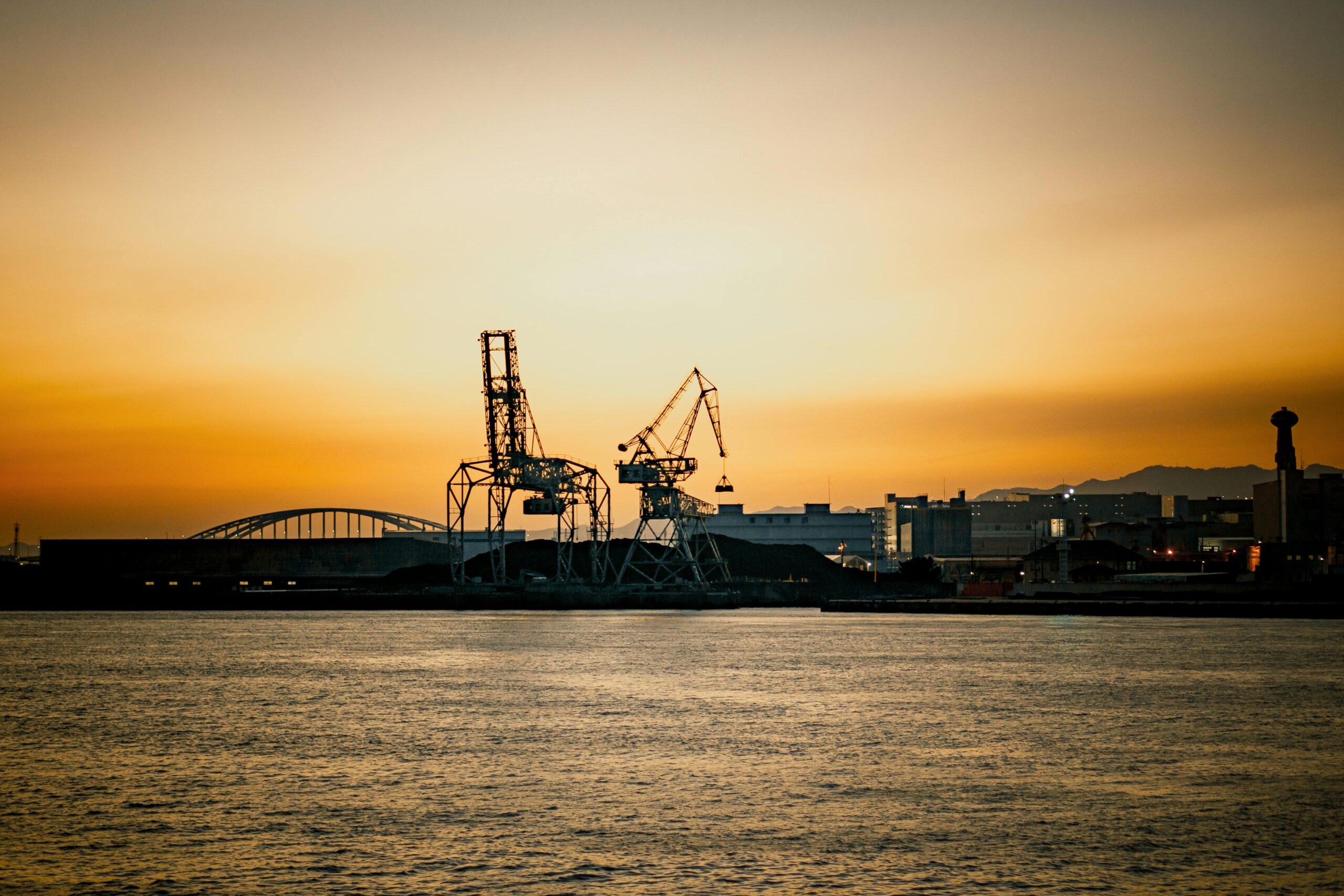Industrial cranes at Osaka Harbor silhouetted against a vibrant sunset sky.