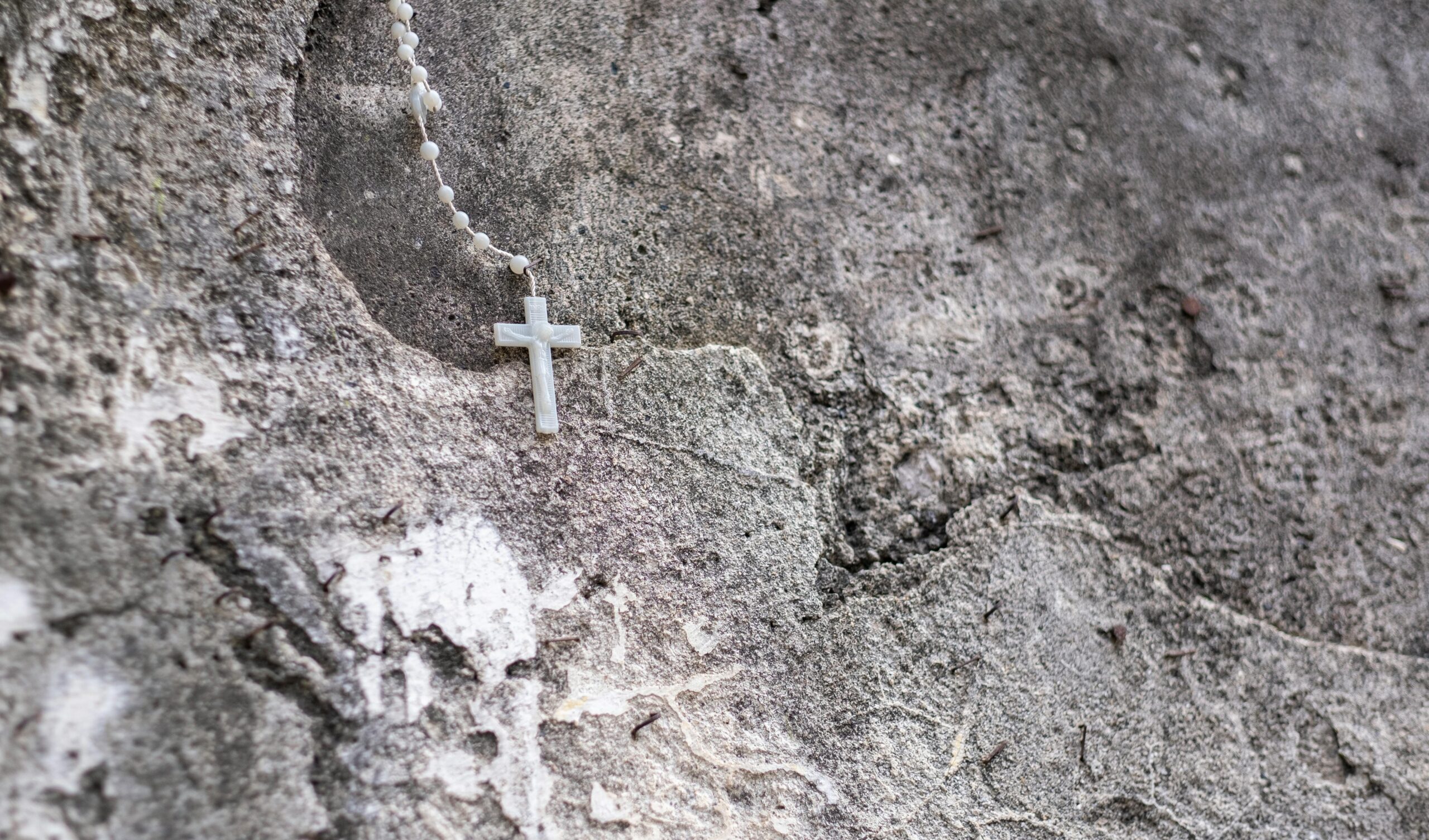 A serene religious scene with a rosary on a textured stone wall in Campania, Italy.